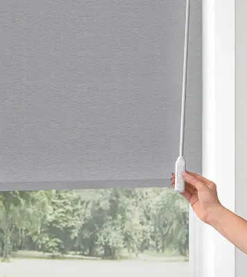 Hand adjusting gray window roller shade.